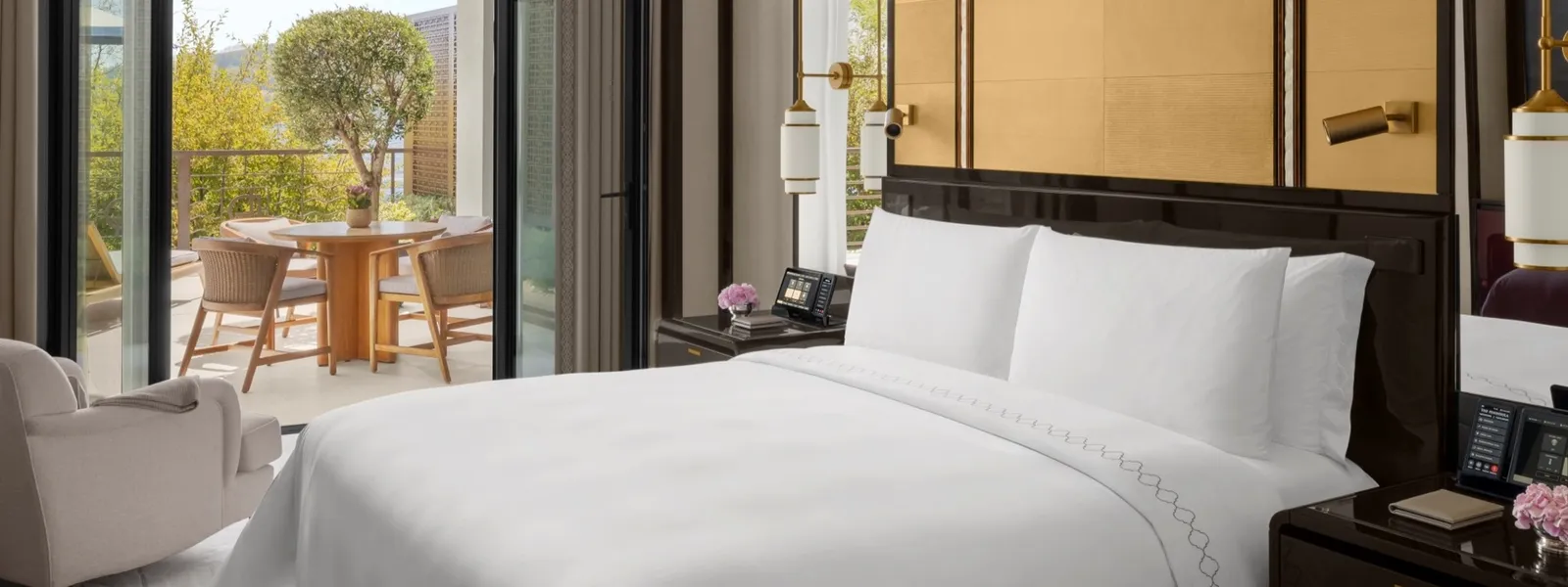 An Executive Bosphorus Suite with Balcony bedroom: the king bed and the door open to the balcony, with a round table, wooden chairs and a potted tree.