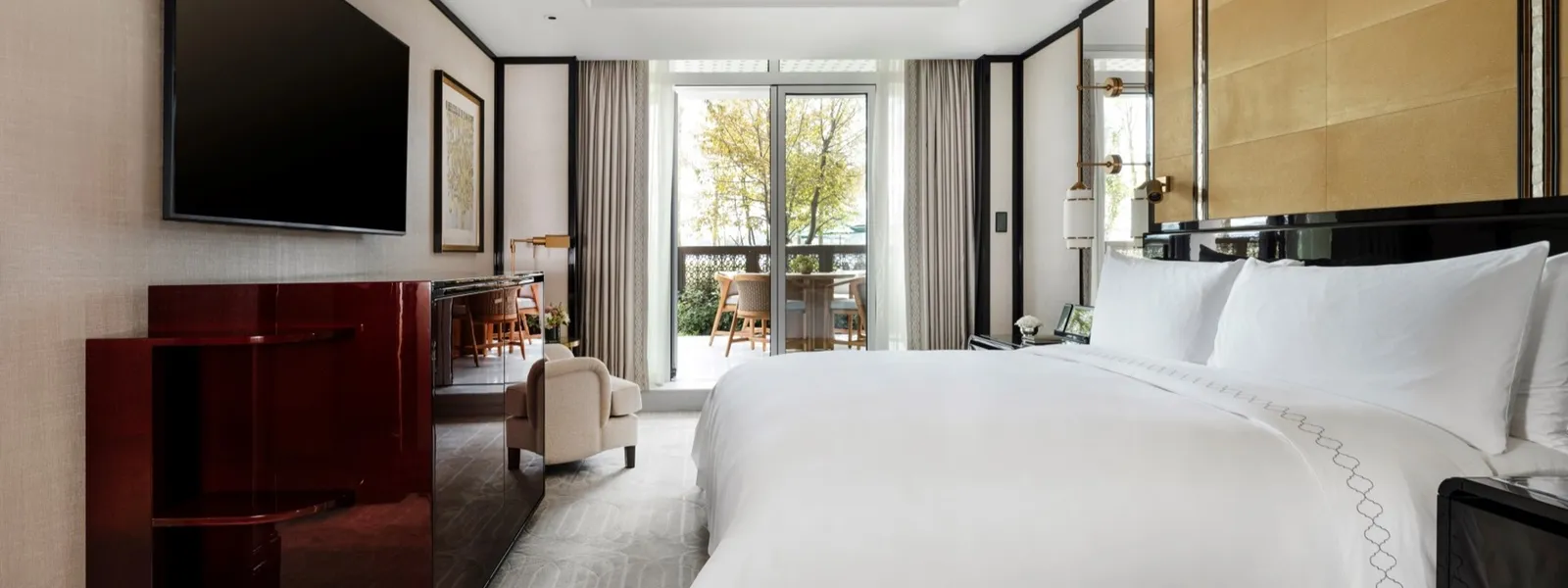 An Executive Bosphorus Suite with Terrace bedroom: the king bed, the television above a red lacquered cabinet and the French window open onto the terrace with its table and chairs.