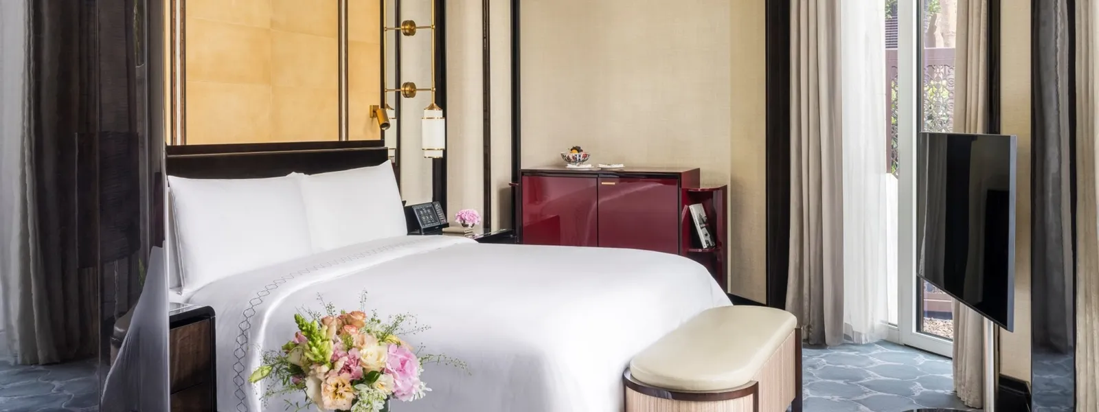 A Grand Deluxe Room with Garden: the king bed, a red lacquered cabinet, the television on a stand and the French window to the terrace.
