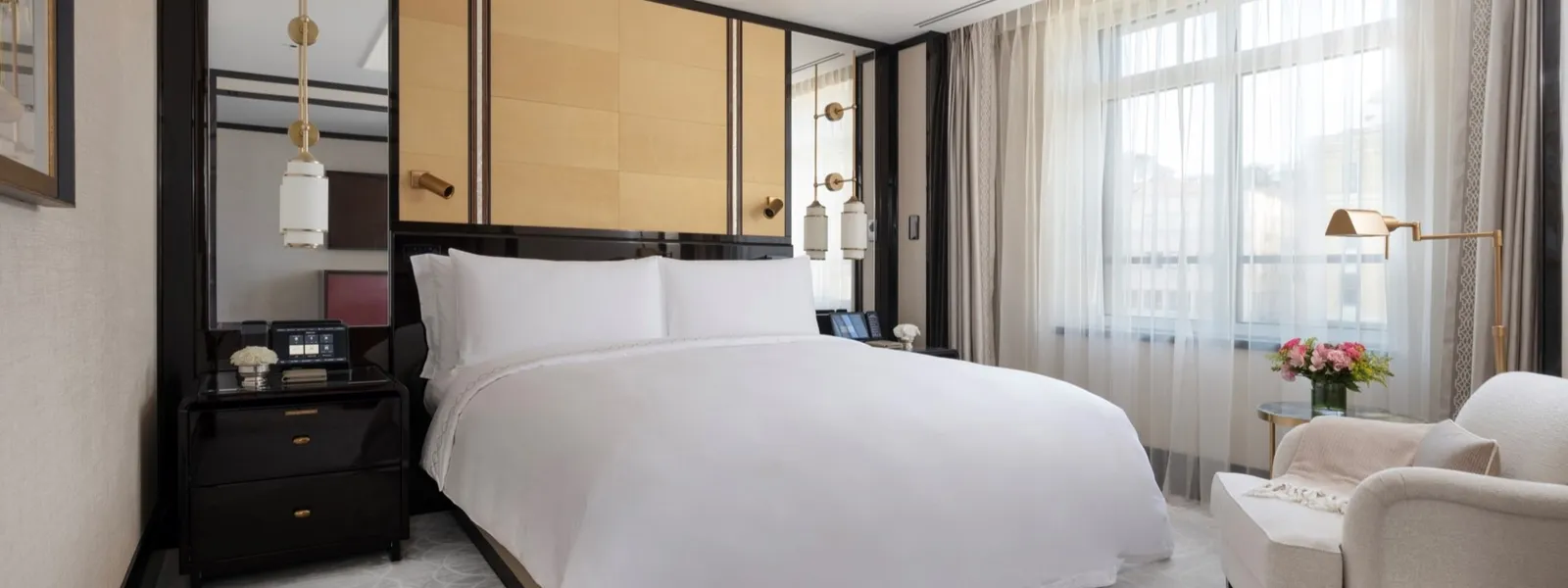 A Superior Suite bedroom: the king bed, dark bedside tables, a pale armchair with flowers beside it and windows behind light curtains.