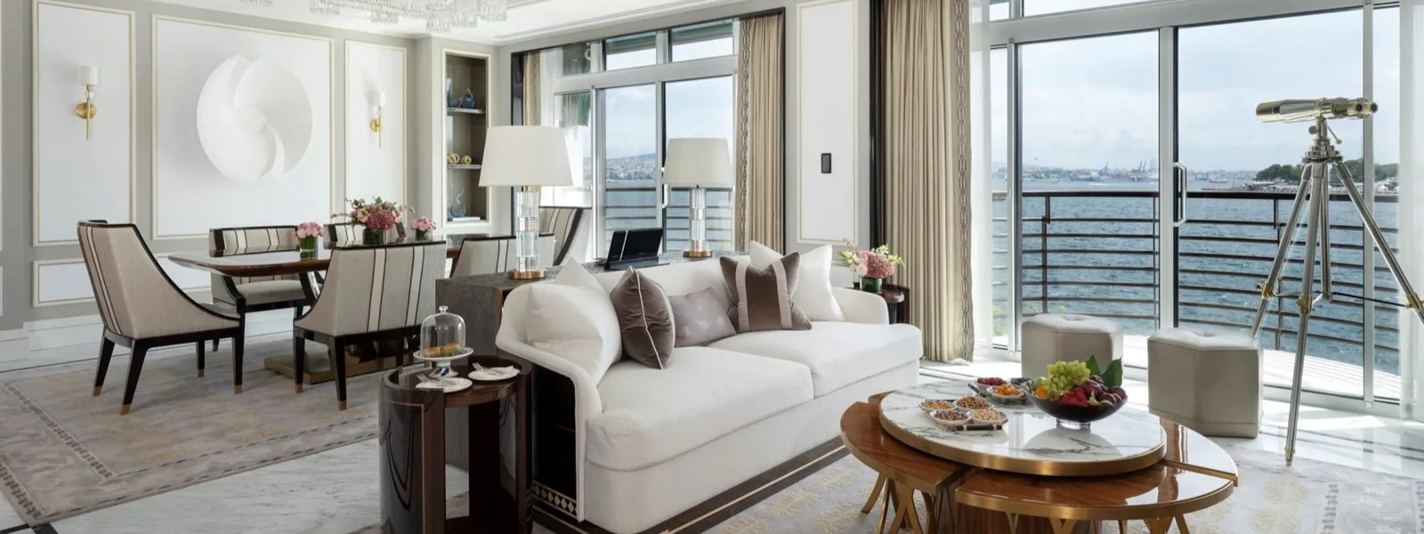 The Art Suite’s living room: a white sofa, the dining table beyond, a white relief on the wall and a telescope at the window over the Bosphorus.