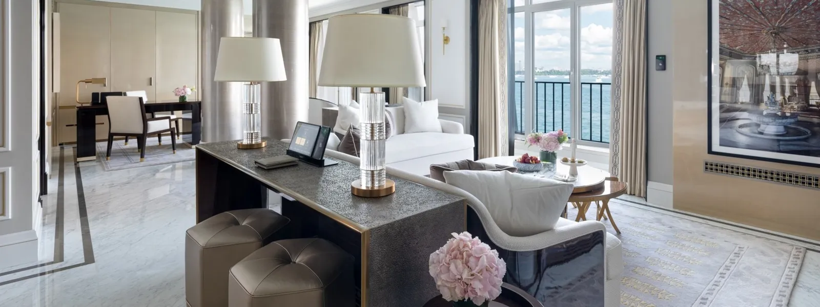 The Rooftop Garden Suite’s living room: a console with 2 lamps behind the sofa, the desk beyond, a marble floor and French windows onto the water.
