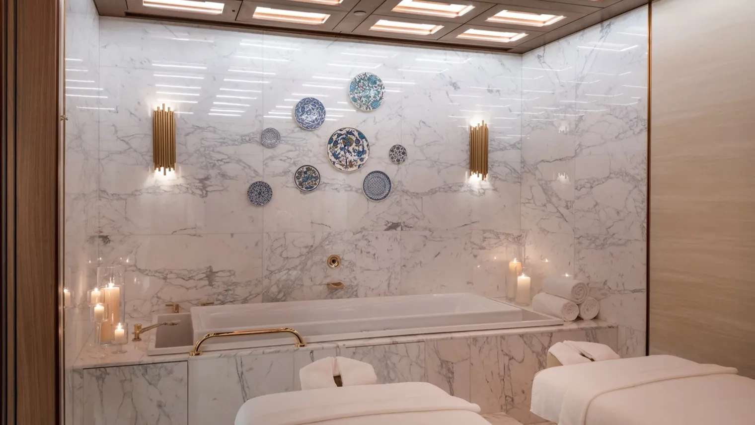 A double spa suite: 2 treatment beds, a marble bath with lit candles and blue ceramic plates hung on the marble wall.