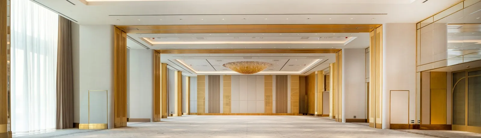 The Yalı Ballroom empty: a long pale hall with gilded portals in sequence, a chandelier at the far end and curtained windows.