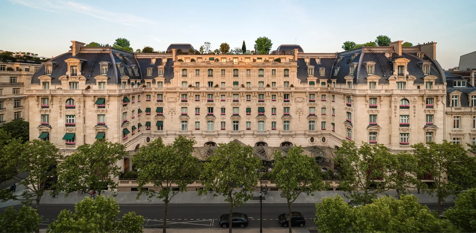 The façade of The Peninsula Paris, with trees along the street and cars outside the entrance