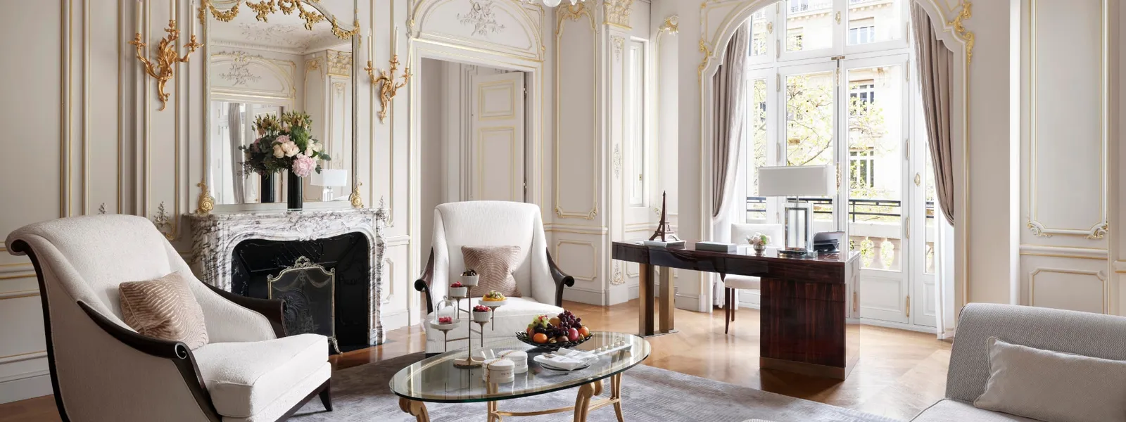 The Historic Suite living room with a gilded mirror, fireplace and pale armchairs