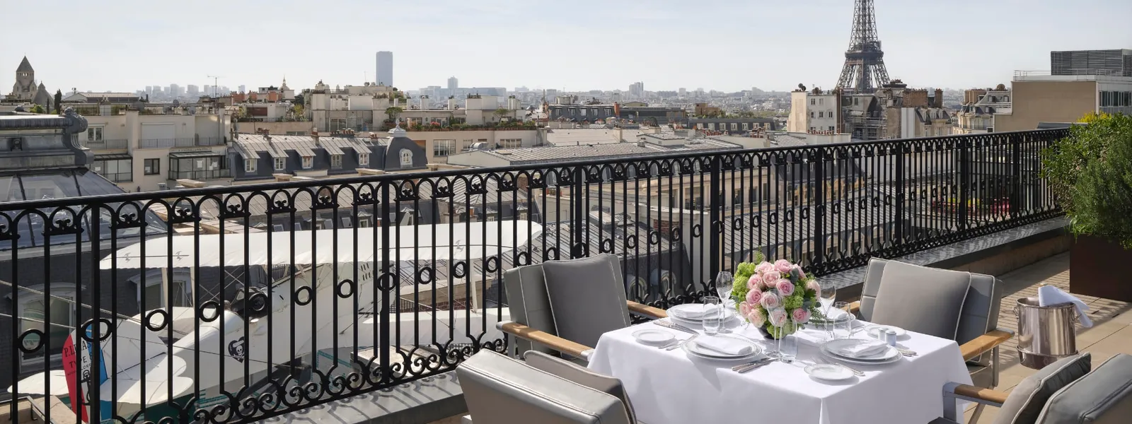 The Rooftop Eiffel Suite terrace with a laid table and the Eiffel Tower beyond the rooftops