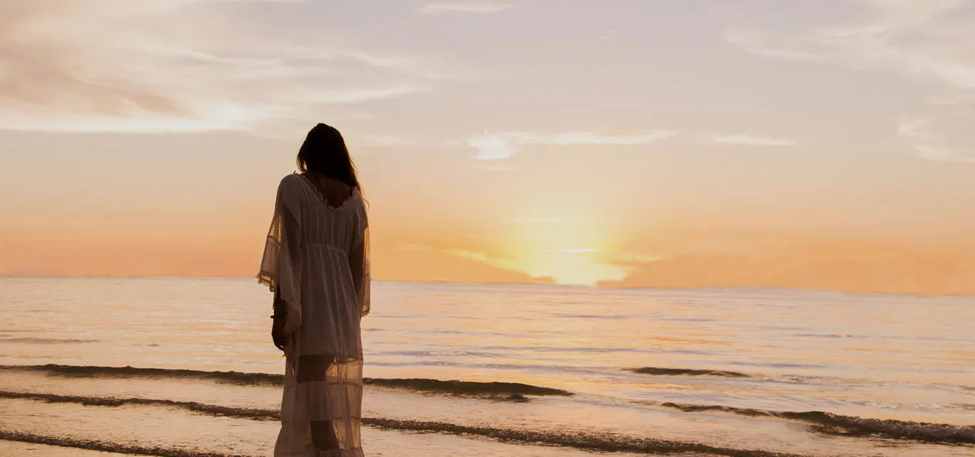 A woman on the shore watches the sun set over the sea