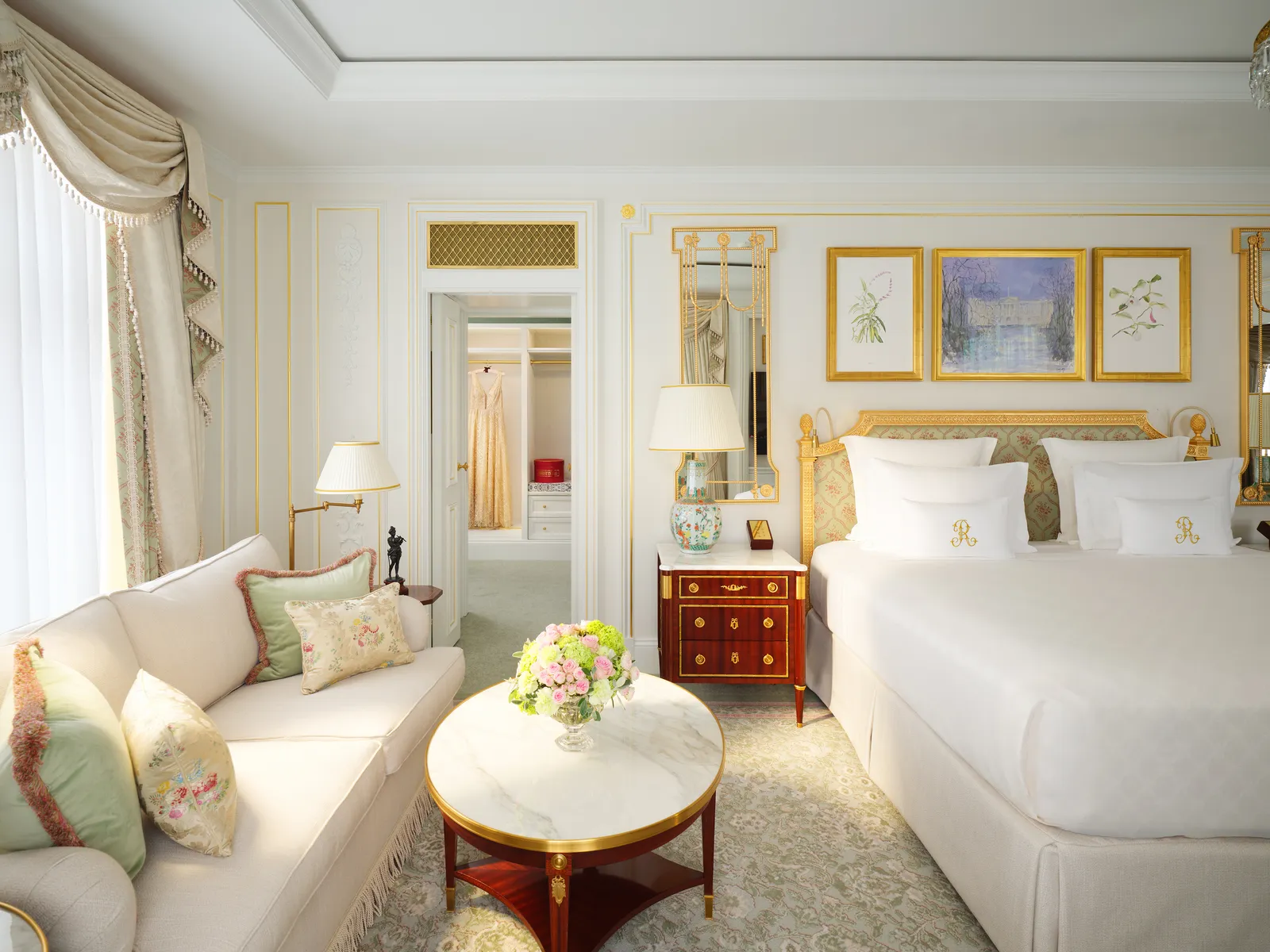 A Grand Deluxe Room: a cream sofa, a round marble table with flowers, a white bed and gilded pictures