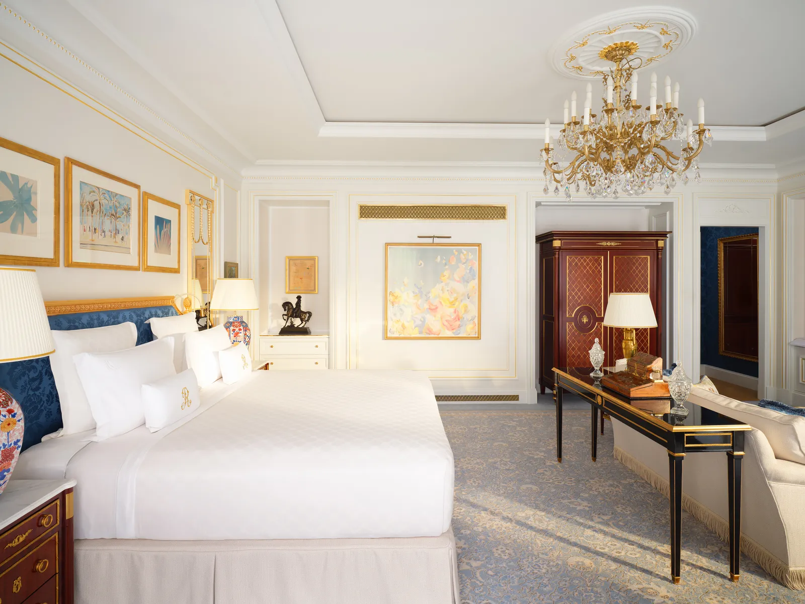 Una Junior Suite: letto bianco con cuscini blu, scrittoio, armadio antico e lampadario di cristallo