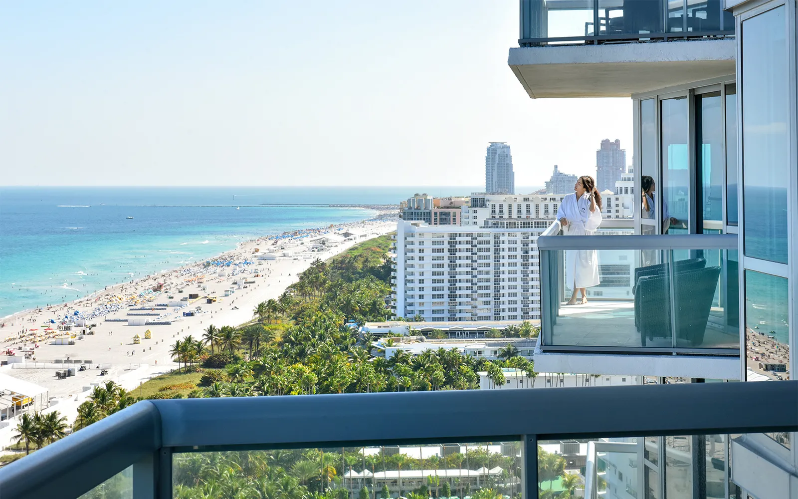 A woman in a bathrobe on an Ocean Suite balcony, above South Beach’s sand running south.