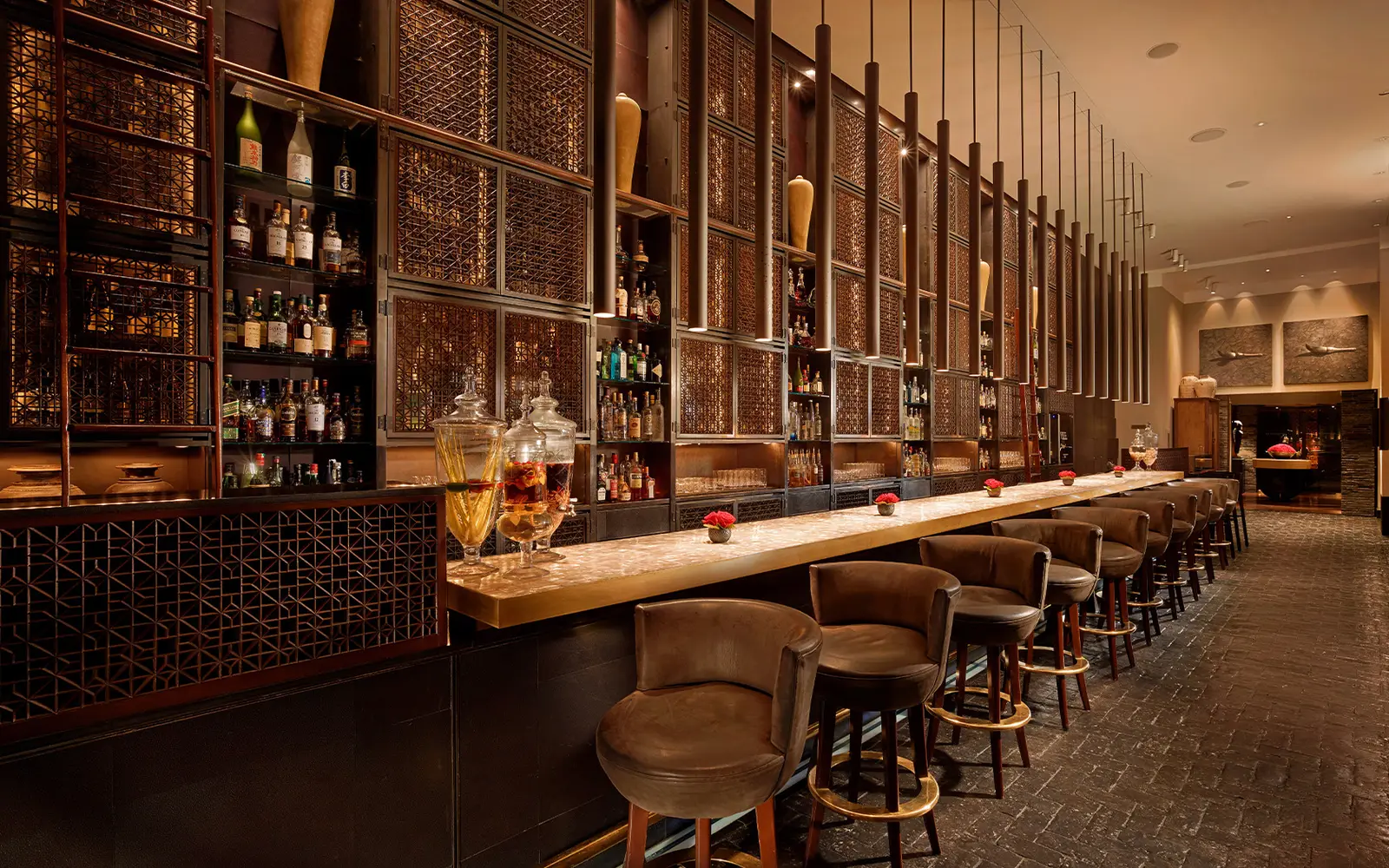 The lobby bar, with its long pale counter, leather stools and bottles against a wall of pierced timber.