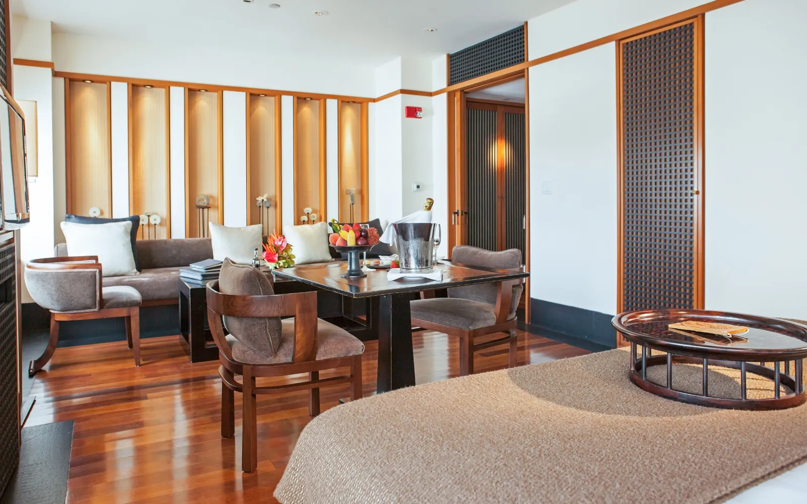 A Studio Suite by day, with a dining table, a sofa against a wall of lit niches and polished wood floors.