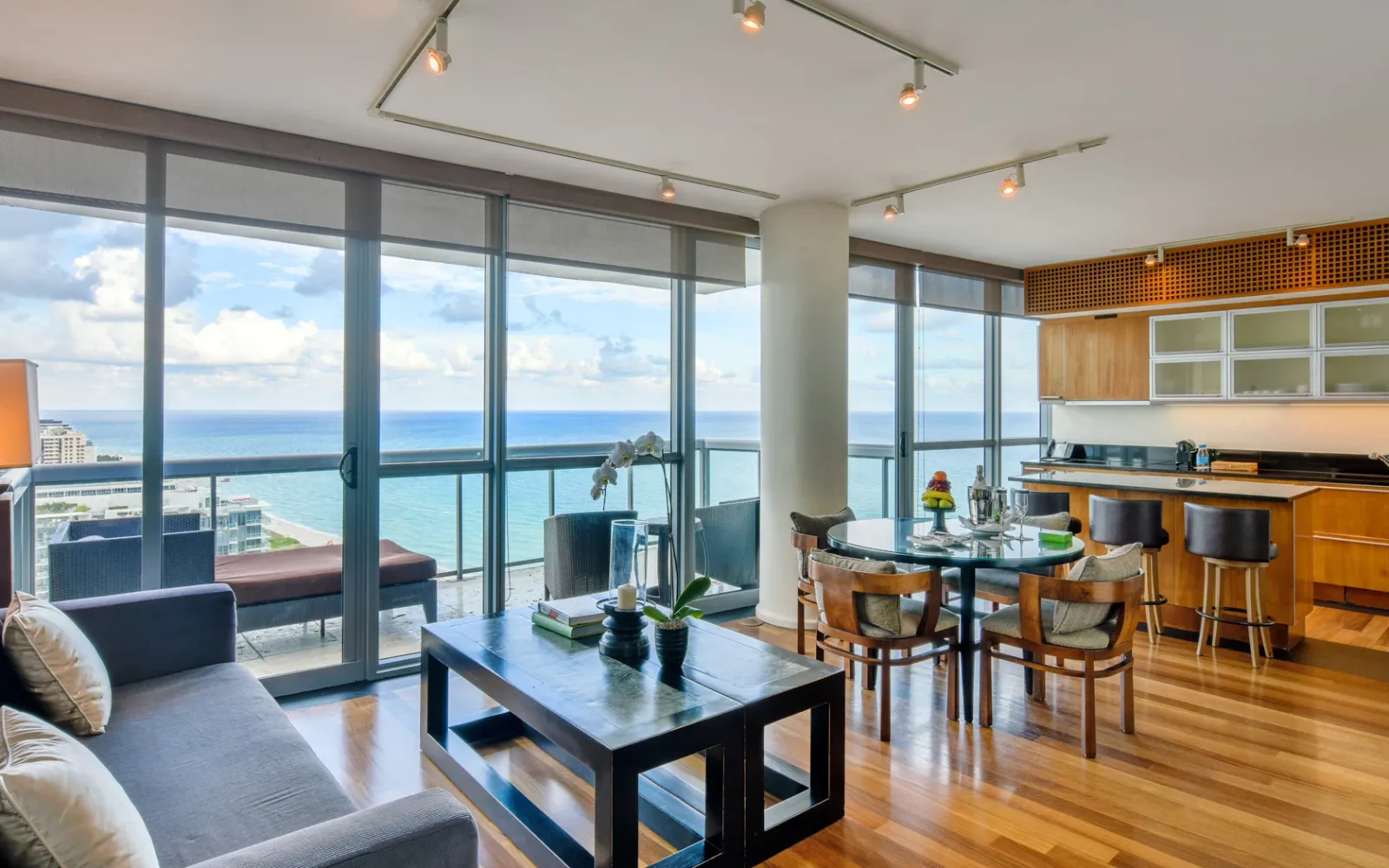 The Entertainment Suite’s living room: sofas, a dining table, the kitchen with its island and the ocean beyond the glass.