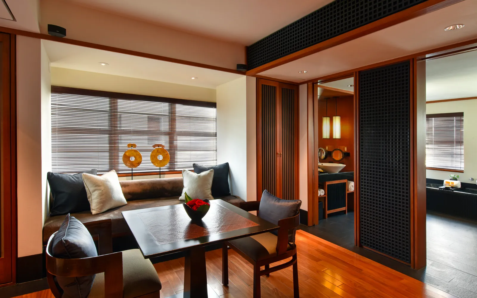 A Junior Suite’s sitting area, with the sofa under a slatted window, a square table and dark timber doors.