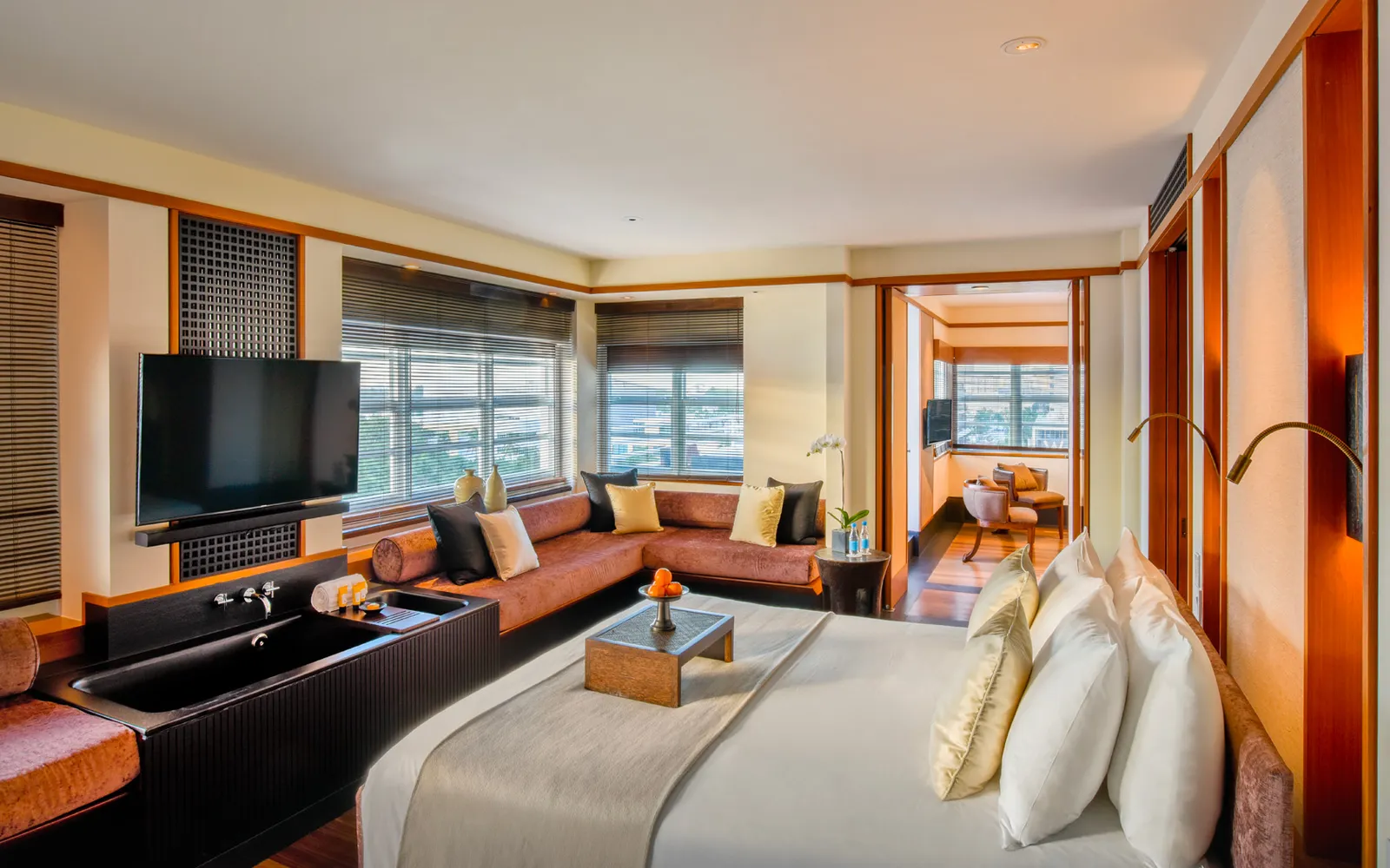 A One Bedroom Suite’s bedroom: the bed with pale cushions, the sunken black bath and a corner sofa under the windows.