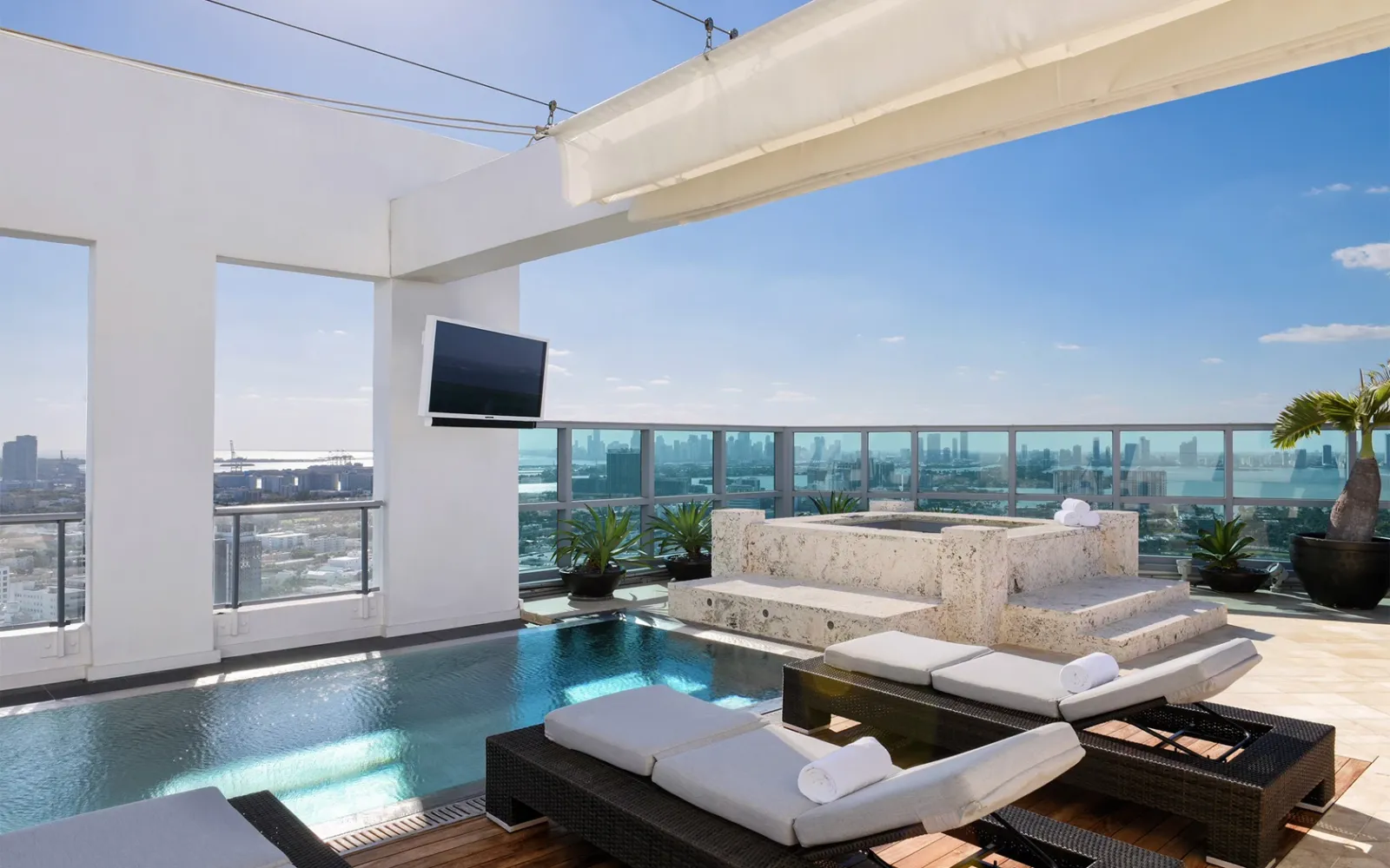The Penthouse terrace: the infinity pool, white daybeds and the city on the horizon under a blue sky.