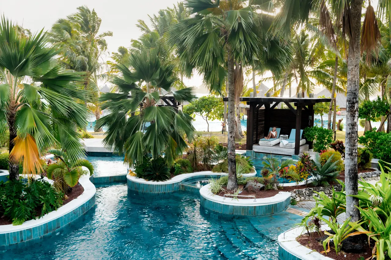 The adults-only Oasis Pool winding between palms towards a cabana