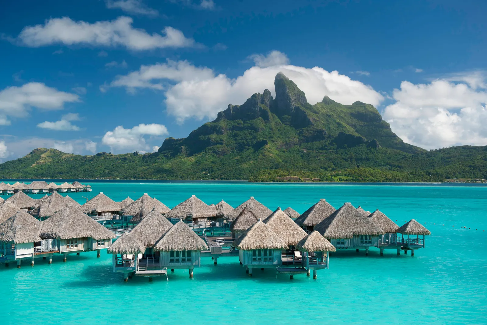 A row of thatched overwater villas on the turquoise lagoon, Mount Otemanu behind