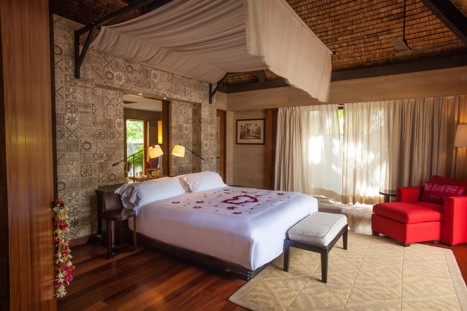 A canopied bed and a red armchair under a woven ceiling