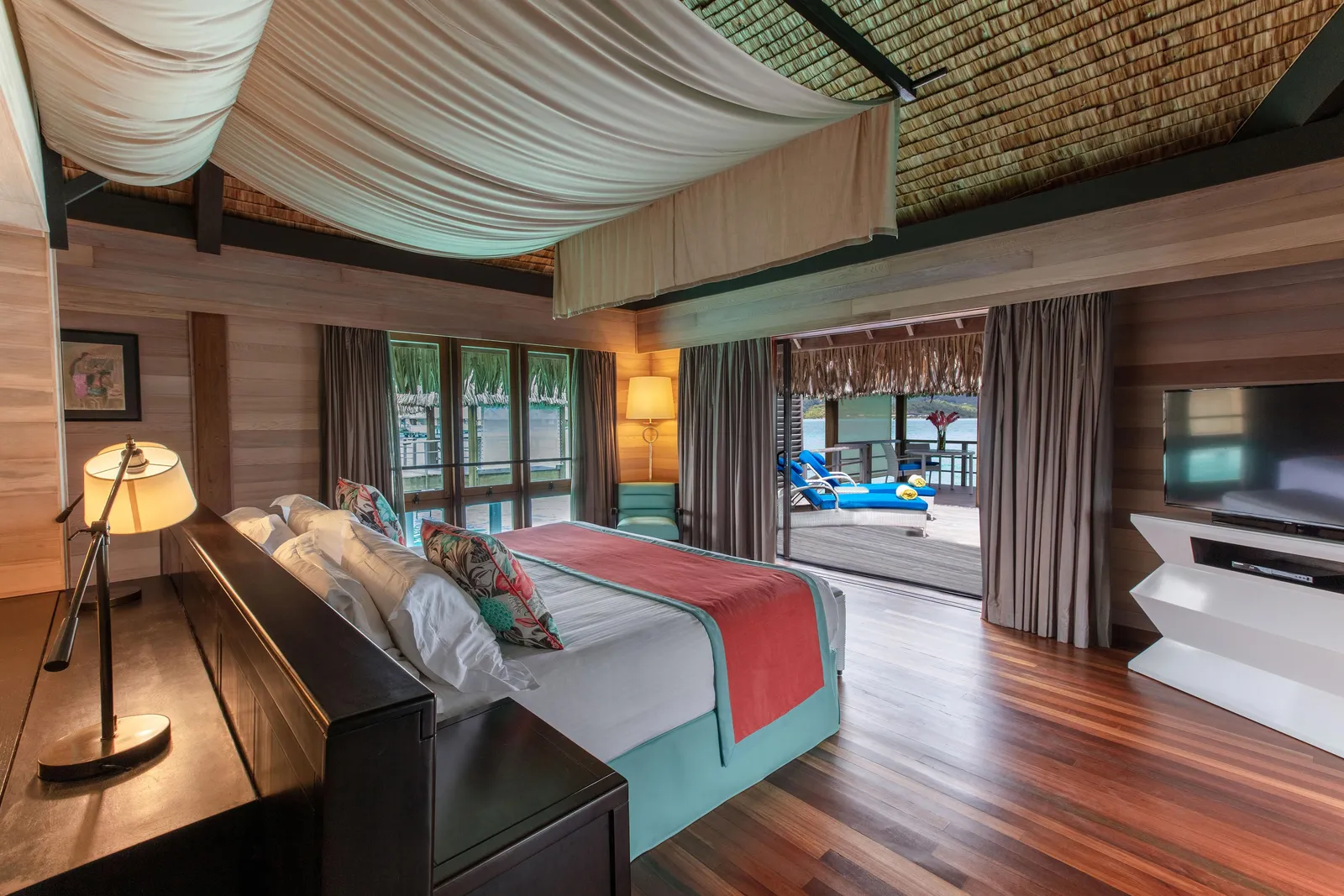 The bedroom, its sliding doors open on the deck and the lagoon
