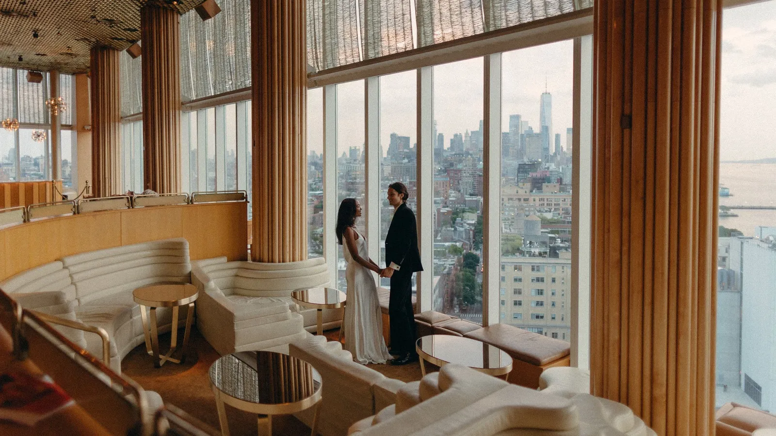 The gold eighteenth-floor room with white armchairs and Lower Manhattan beyond the glass