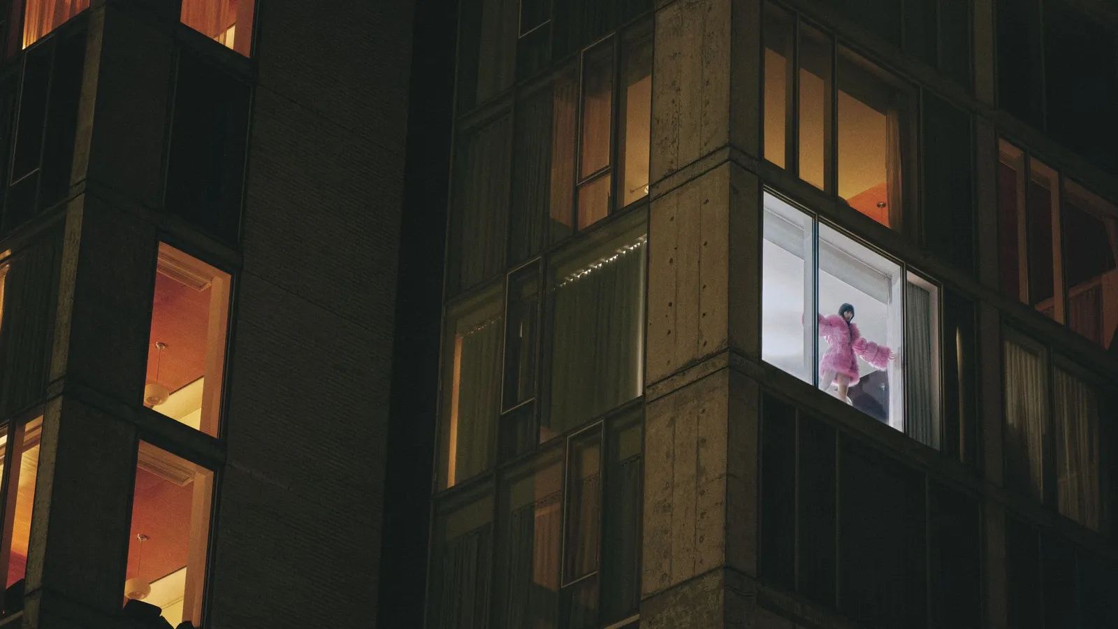 The façade at night, a grid of lit windows and a figure in one room