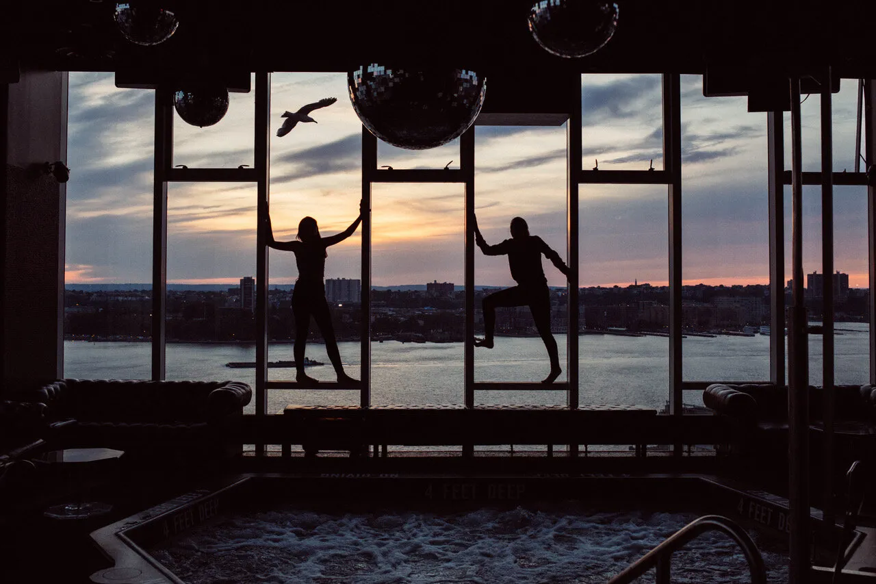 2 figures silhouetted in Le Bain’s windows at sunset, the plunge pool and the Hudson below