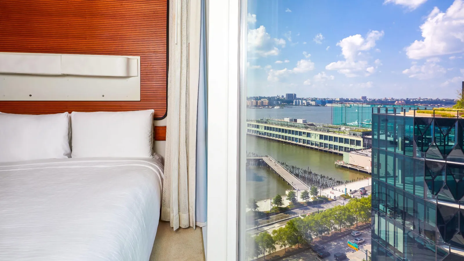 A Standard Queen: the white bed beside the glass wall, the Hudson and the piers below