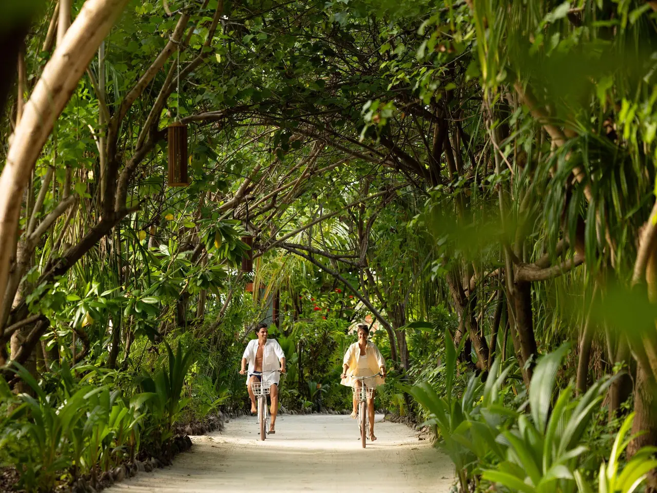 2 guests cycling along a sandy path through the island’s dense greenery.