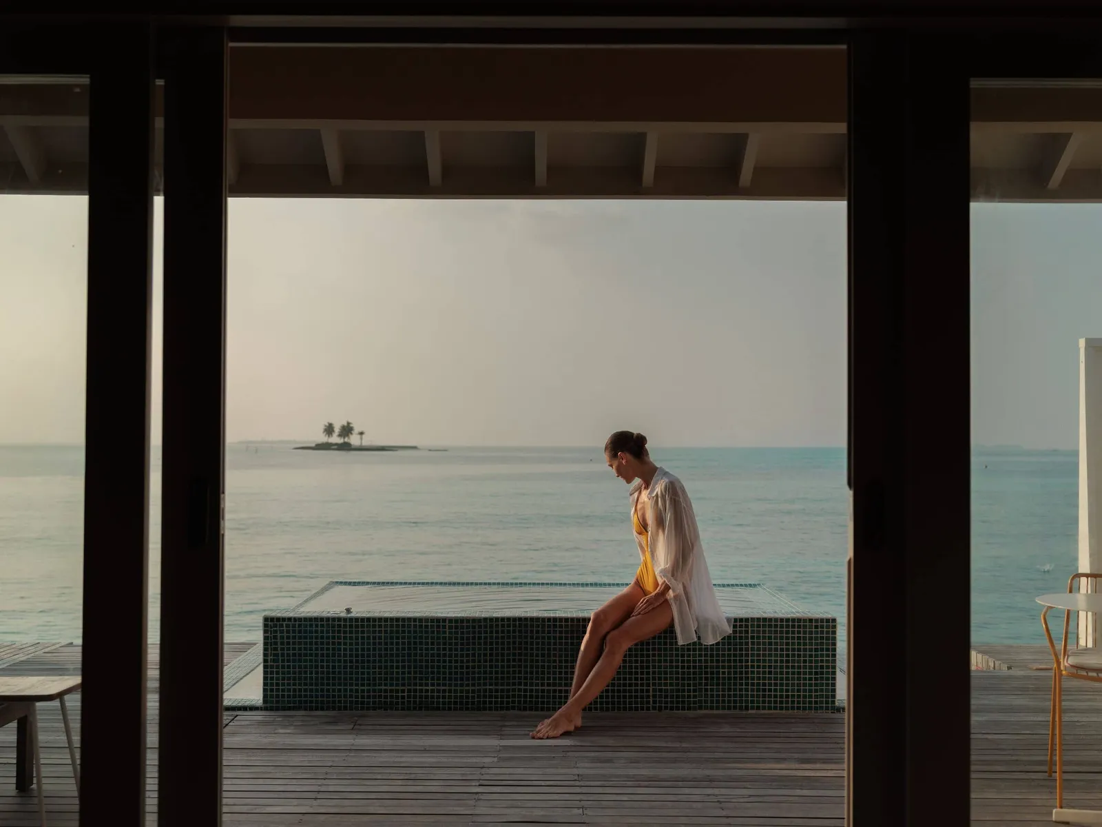A guest sitting on the edge of a water villa’s pool, seen from the room, with the lagoon and an islet ahead.