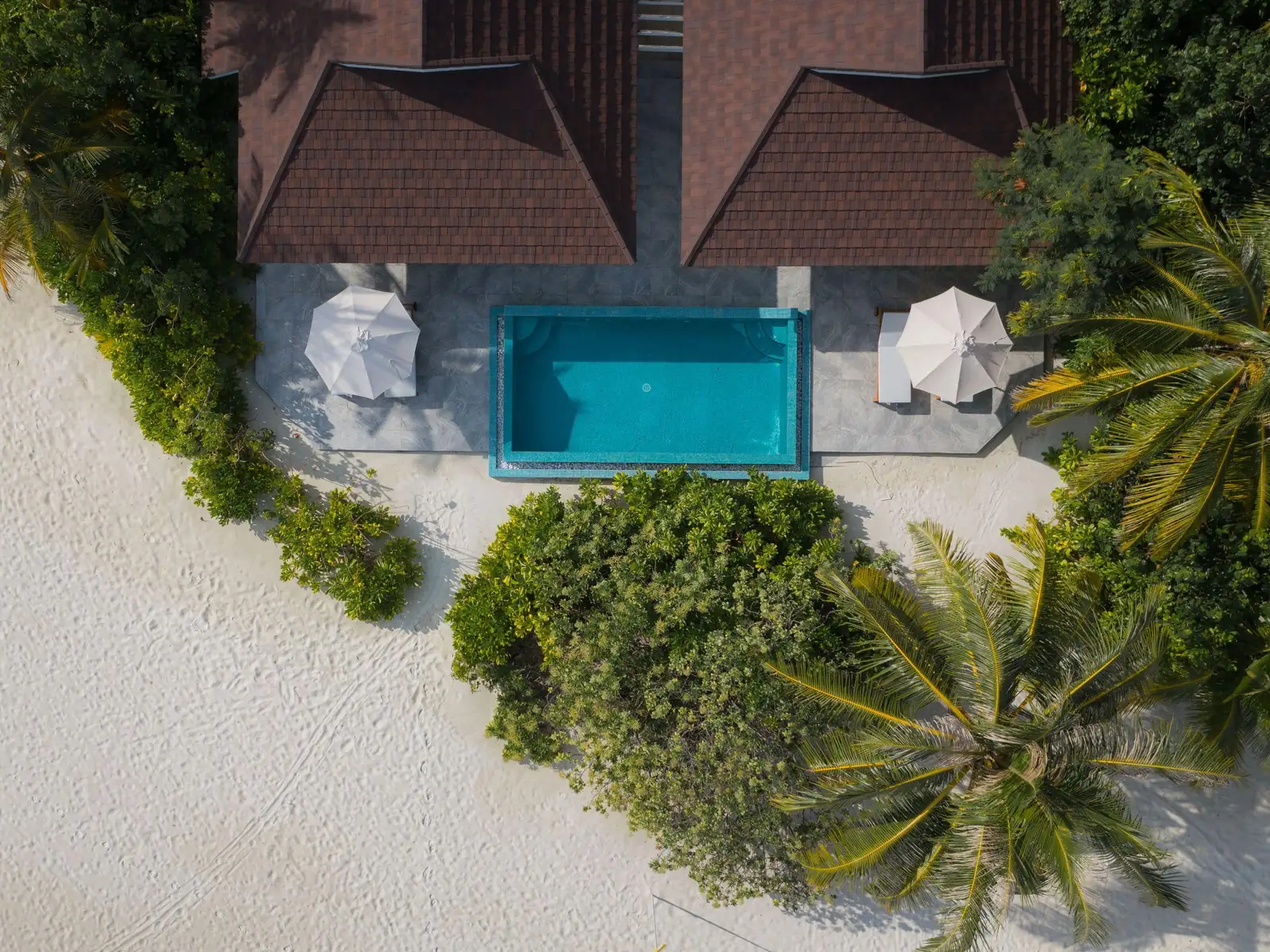 The 2-bedroom beach villa from above: the 2 roofs, the pool between them, the parasols and the sand.