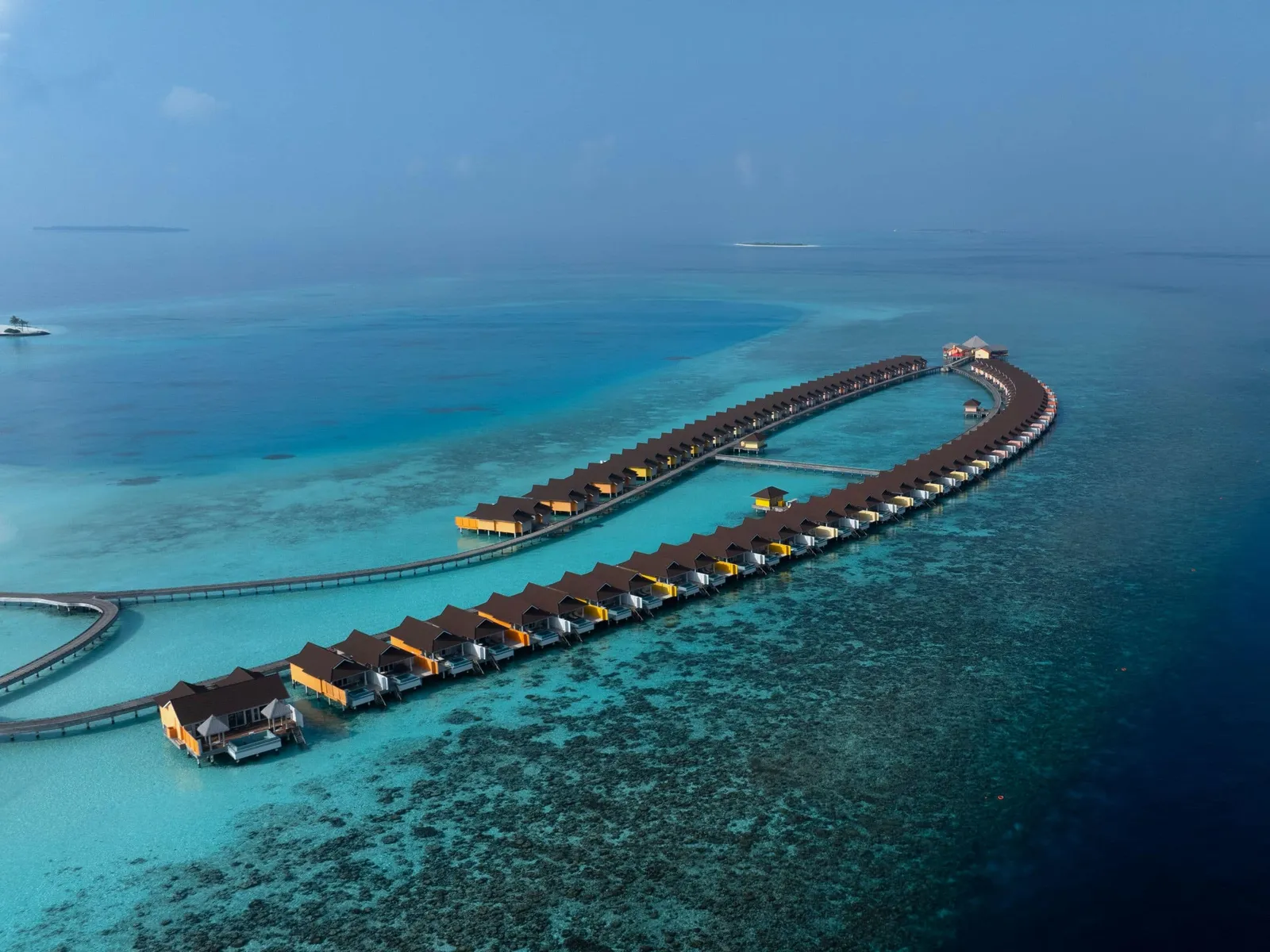 From above, the 2 loops of water villas leaving the island across the turquoise lagoon, the reef around them.