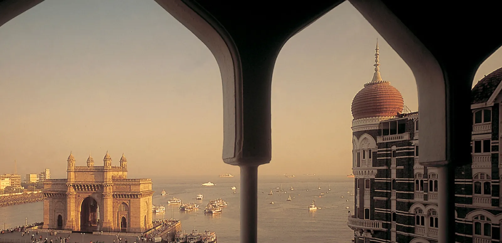 The Gateway of India at sunset framed by an arch of the Taj Mahal Palace, its red dome to the right