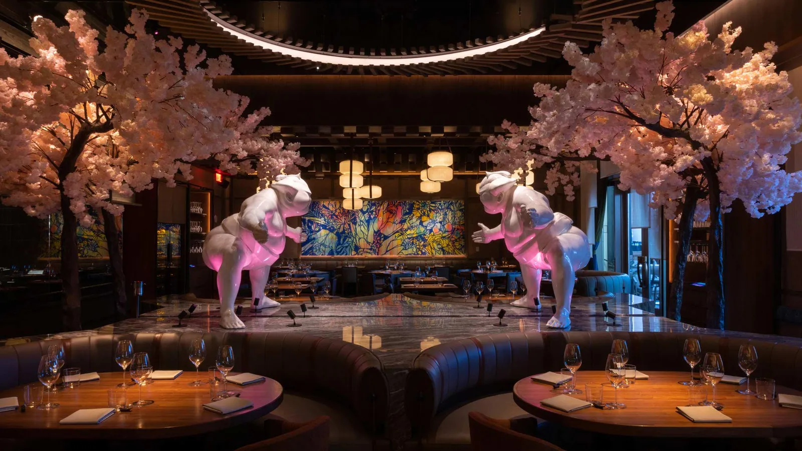 The dining room of WAKUDA at the Palazzo: 2 white sumo sculptures on a marble counter between pink cherry-blossom trees, booths laid for dinner in front