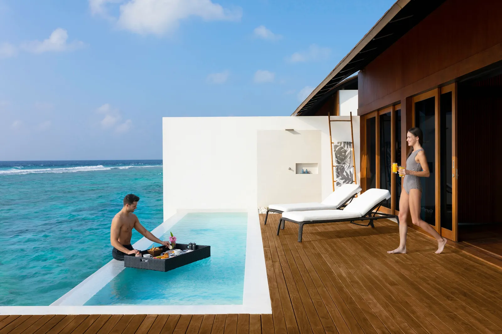 Floating breakfast in a water villa’s private pool, on a black tray, with the sea beyond the edge.