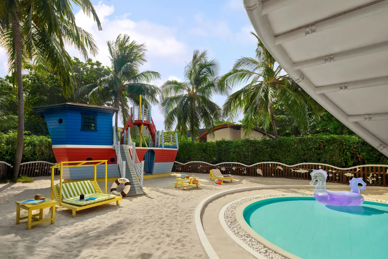 The Kids Club garden: the brightly painted wooden pirate ship, the sand, yellow loungers and the children’s pool with an inflatable unicorn.