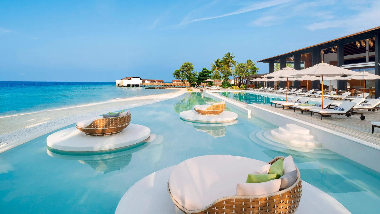 The main infinity pool, with round islands and wicker daybeds in the water and parasols along the edge.