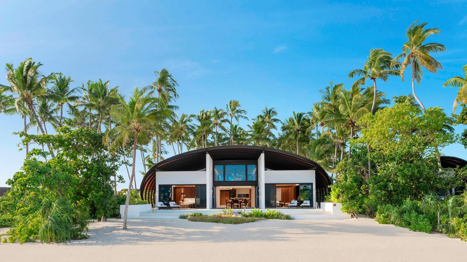 The Heavenly Beach Residence from the beach: the house under its double curved roof, the pool and loungers on the sand.
