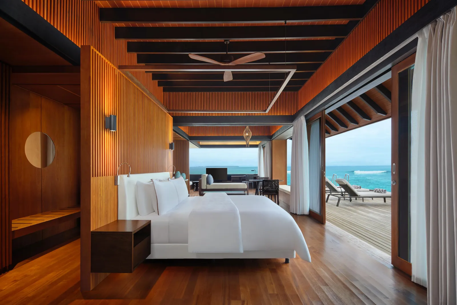 A Heavenly Overwater Villa bedroom, the king bed under the timber ceiling and the deck open on the ocean.