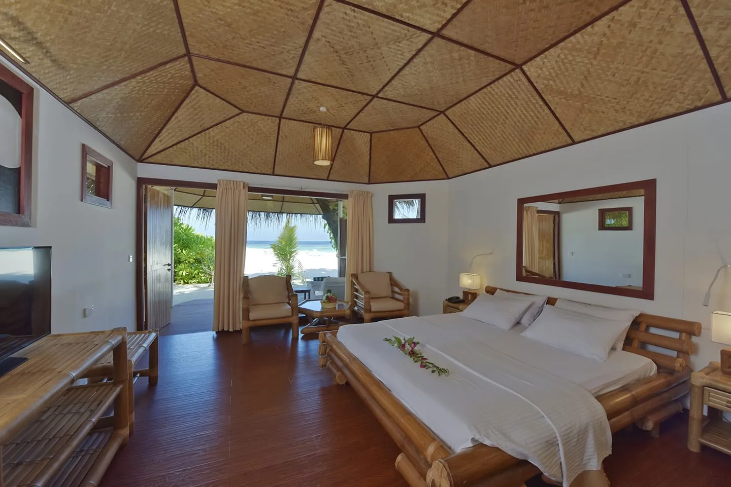 A beach bungalow bedroom: the bamboo bed, the woven ceiling and the door open onto the sand.