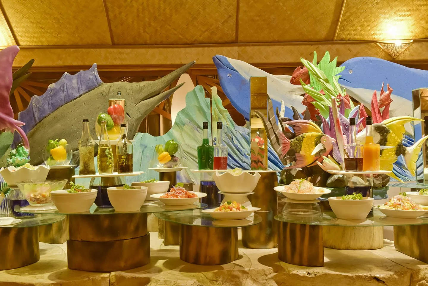 The restaurant buffet: salads and starters on wooden stands, in front of brightly painted fish sculptures.