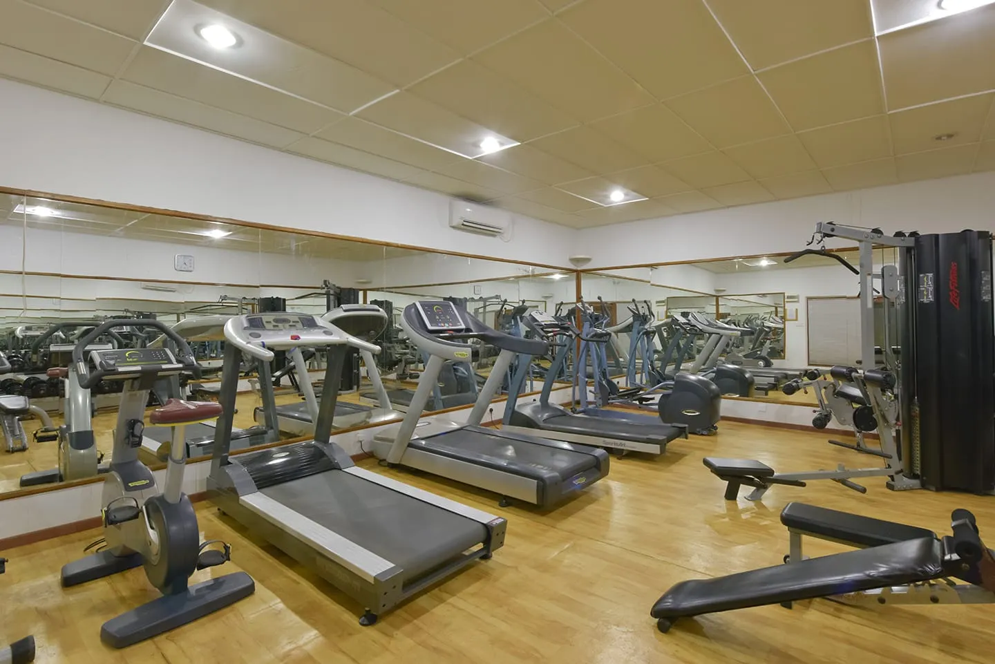 The gym, with treadmills, machines and mirrors under the pale ceiling.