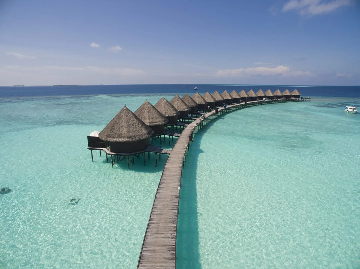 The curving row of thatched water bungalows above the turquoise lagoon, seen from the air.