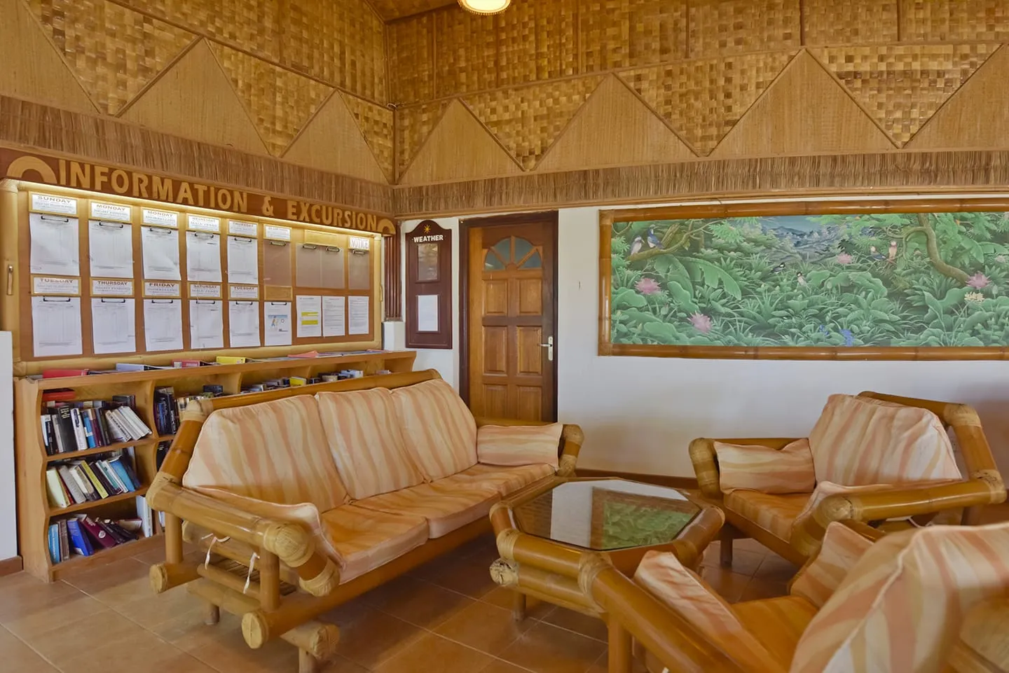 Reception under its woven bamboo ceiling, with the sofas, the bookshelf and the excursions board.