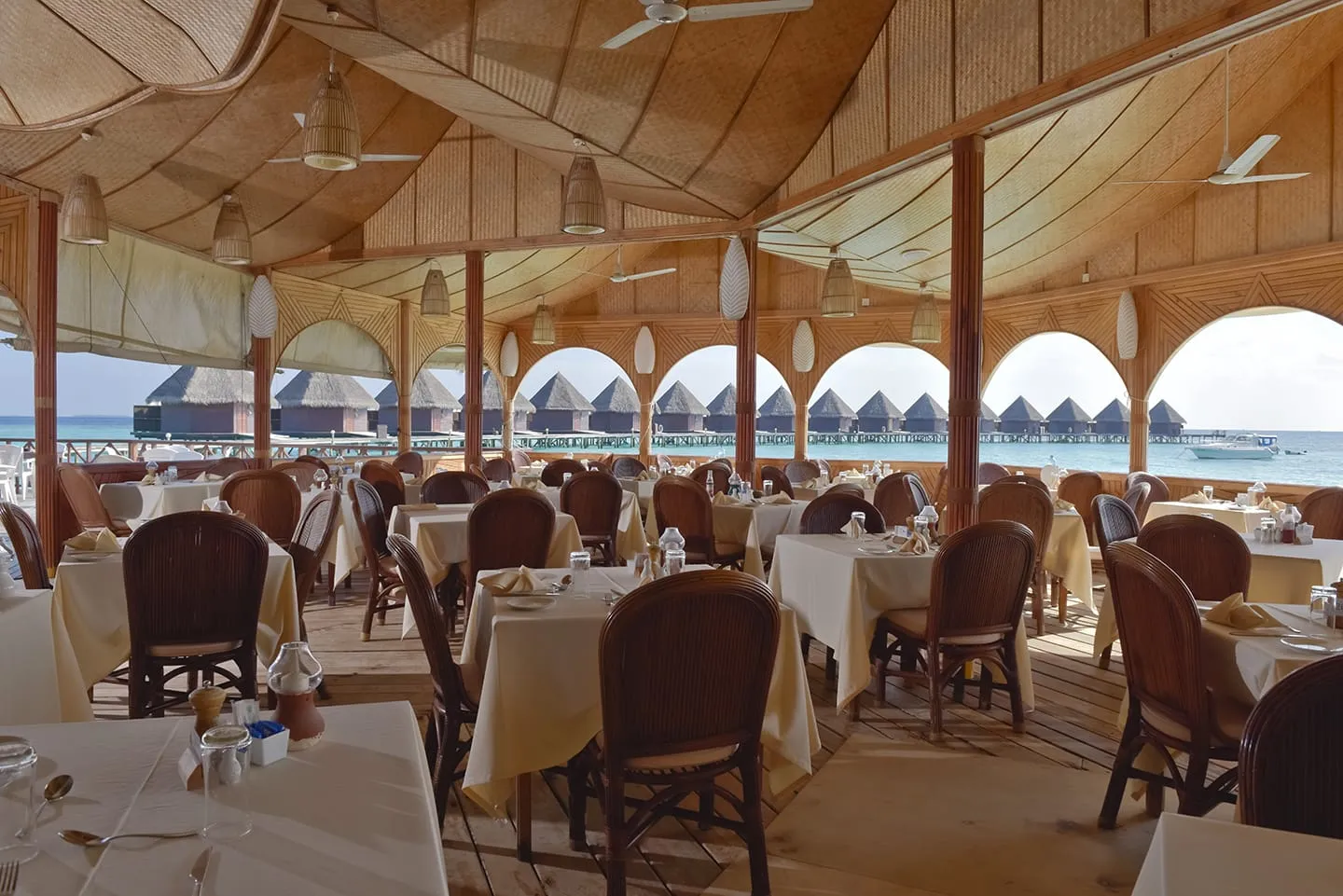 The restaurant under its thatched roof, tables laid and arches open onto the lagoon and the water bungalows.
