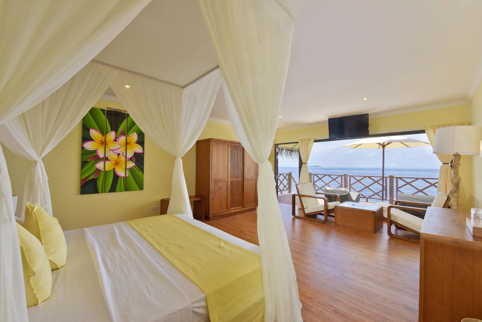 A Superior Water Bungalow bedroom: the four-poster bed with white drapes and the door open onto the deck and the sea.