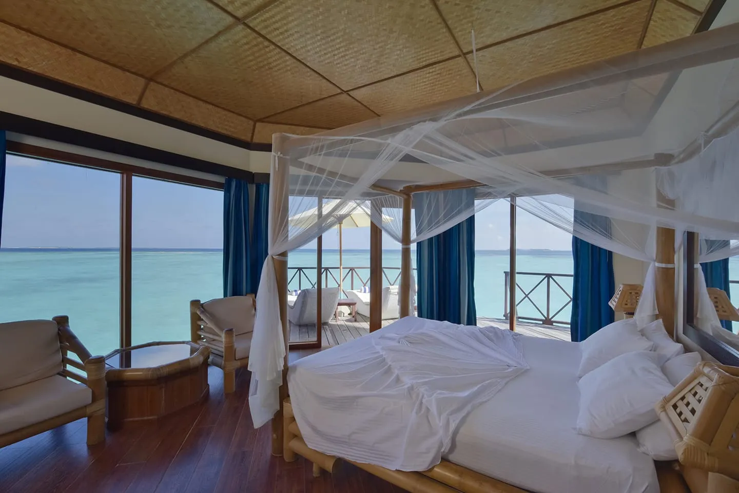 A water bungalow bedroom, the bed under its net and the glass doors onto the deck and the lagoon.