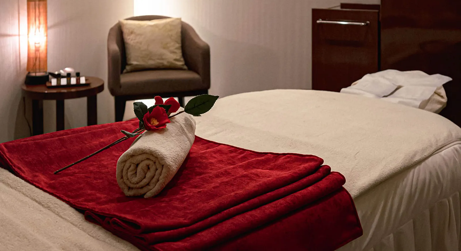 A treatment room at AN Spa: the couch with its red blanket, a rolled towel with a flower and an armchair.