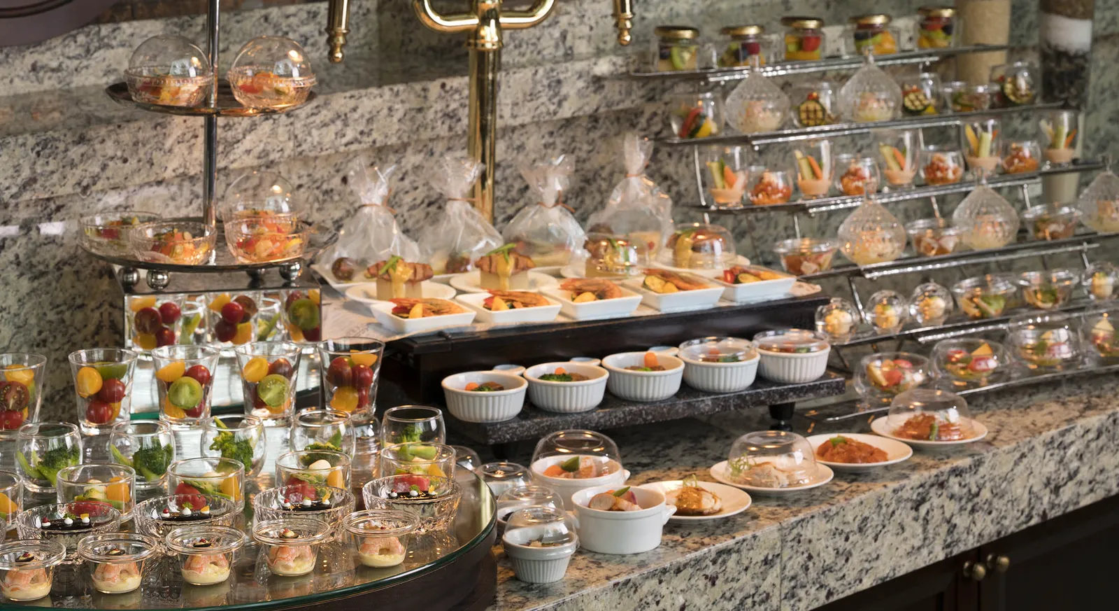 The breakfast buffet at the Atrium: glasses of fruit and vegetables, small hot dishes under glass cloches on a granite counter.